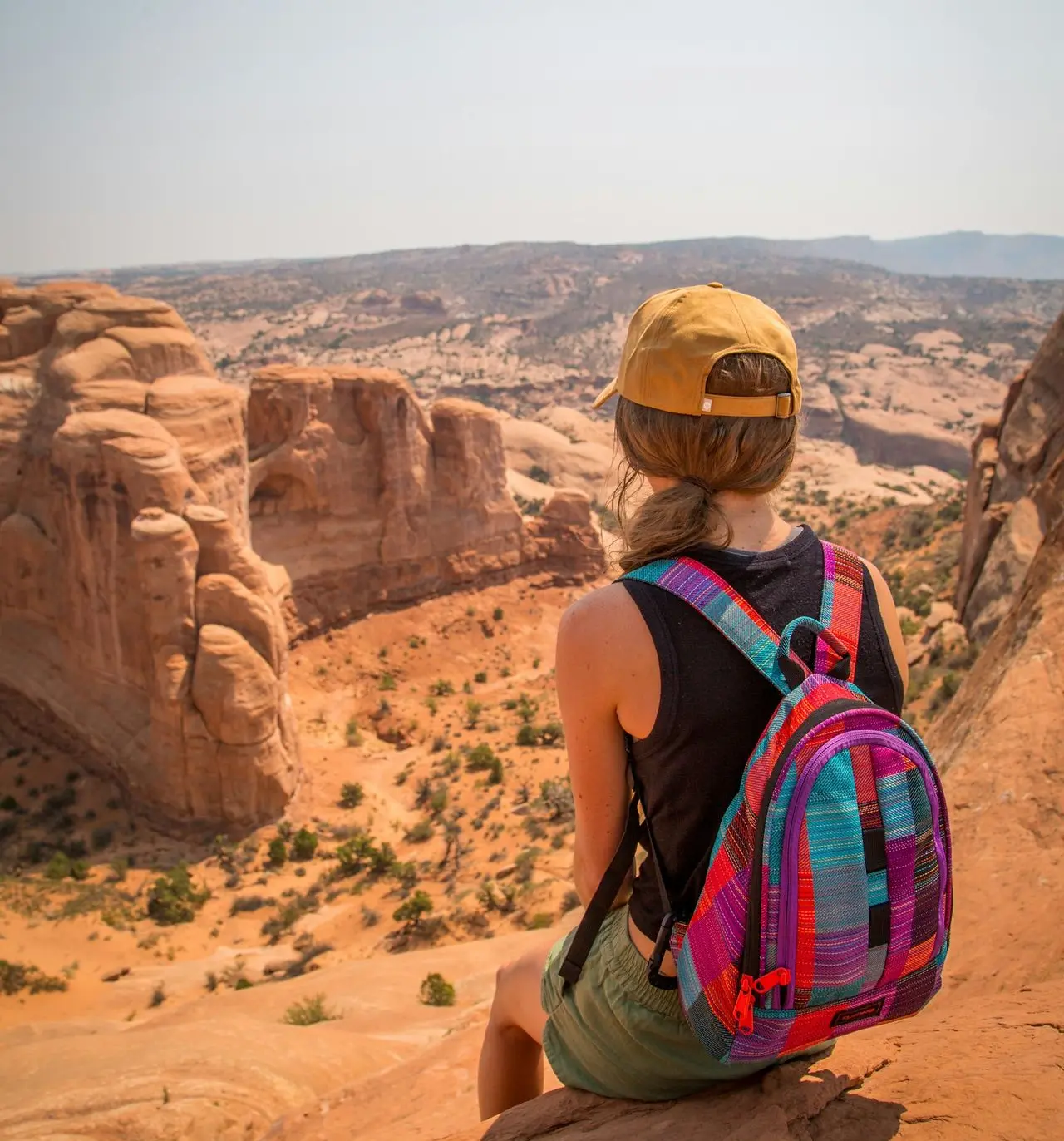 sitting woman carrying backpack overlooking canyon during daytime